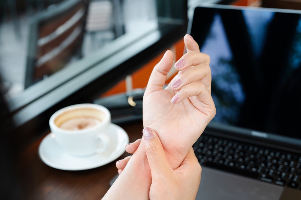 A lady holds her wrist in pain while using a laptop. Carpal Comfort - Designed to Soothe Carpal Tunnel Pain